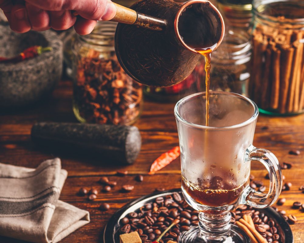 Man Pour Hot Soaring Coffee in Glass Mug. Oriental Spices and Coffee Beans on Metal Tray.